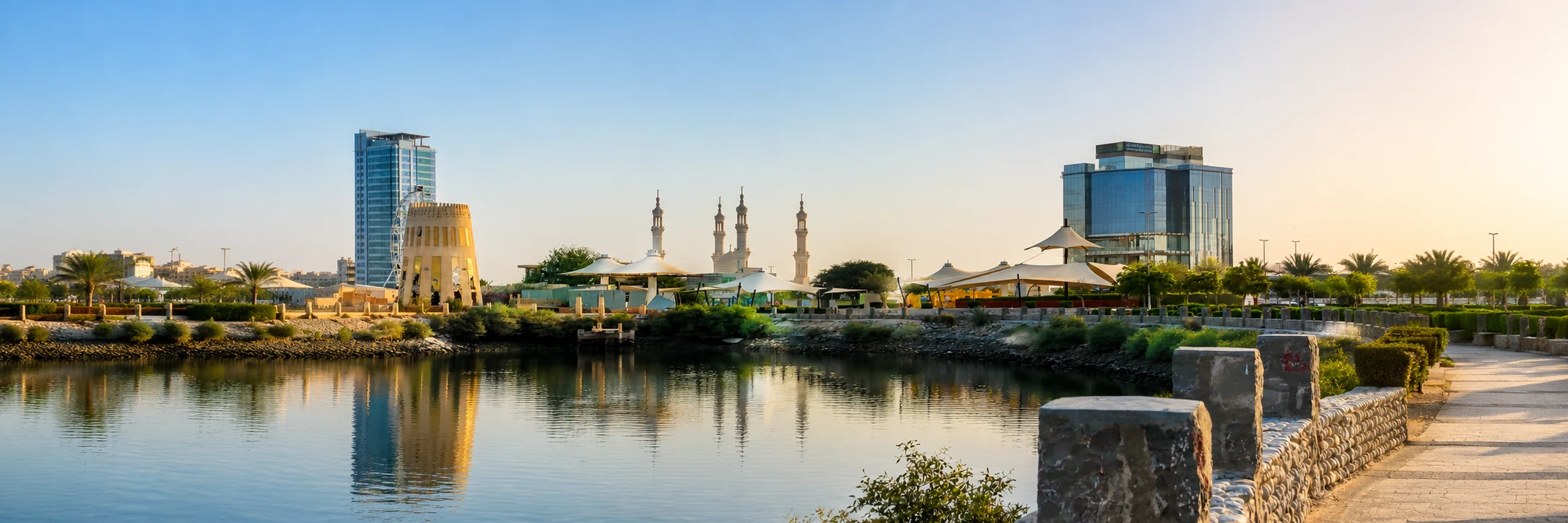Panorama of the Ras Al Khaimah corniche with a mosque, towers and calm water at golden hour